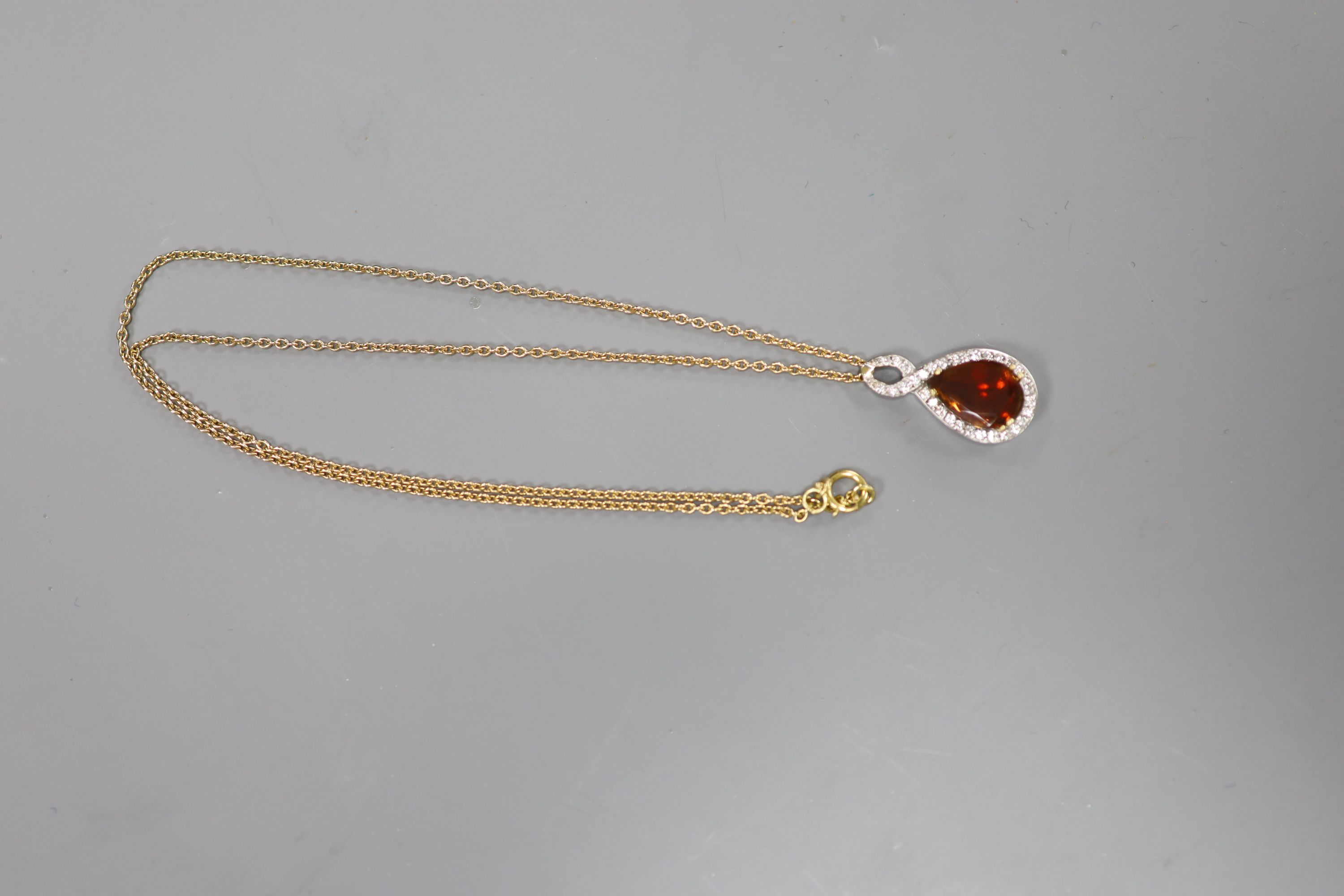 A white and yellow metal, garnet and diamond set teardrop shaped pendant, 29mm, on an 18k fine link chain,